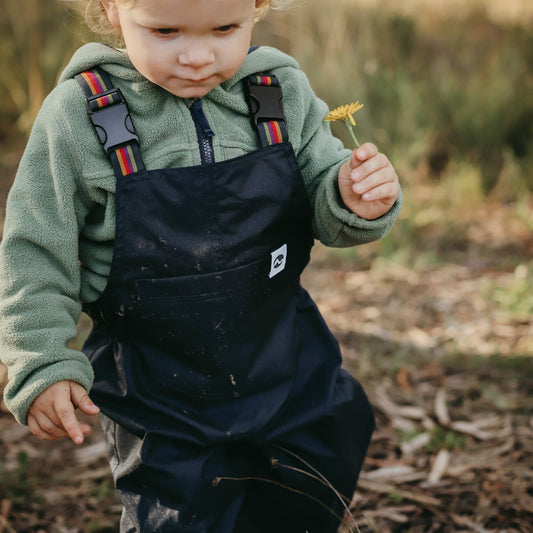 Child in navy waterproof overalls holding a flower outdoors