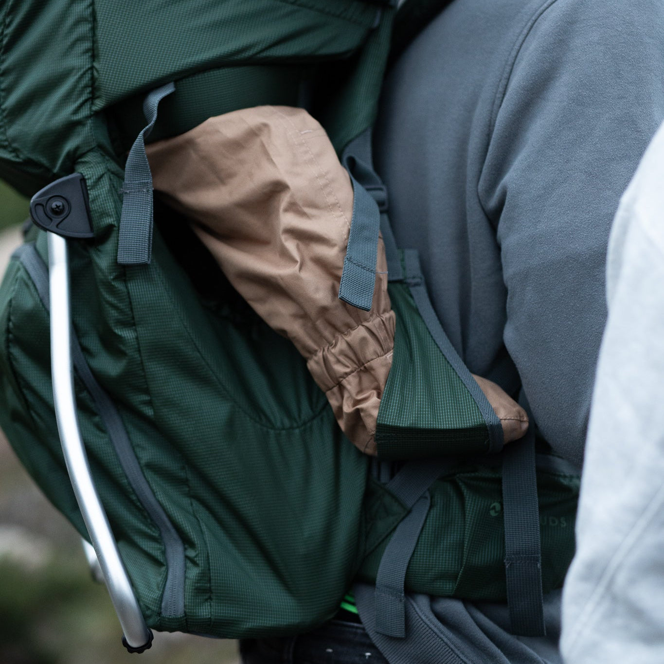 Person wearing a green backpack with a child inside, set against a natural background.