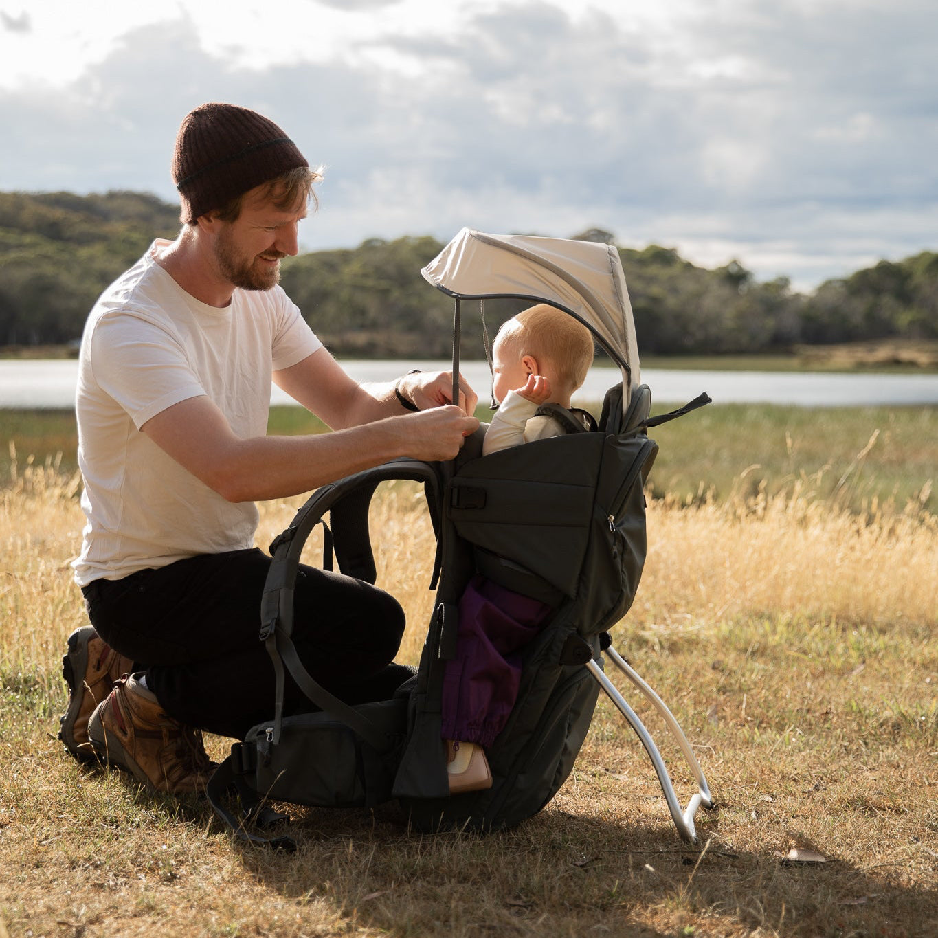 Man sitting with a baby in a stroller outdoors by a lake