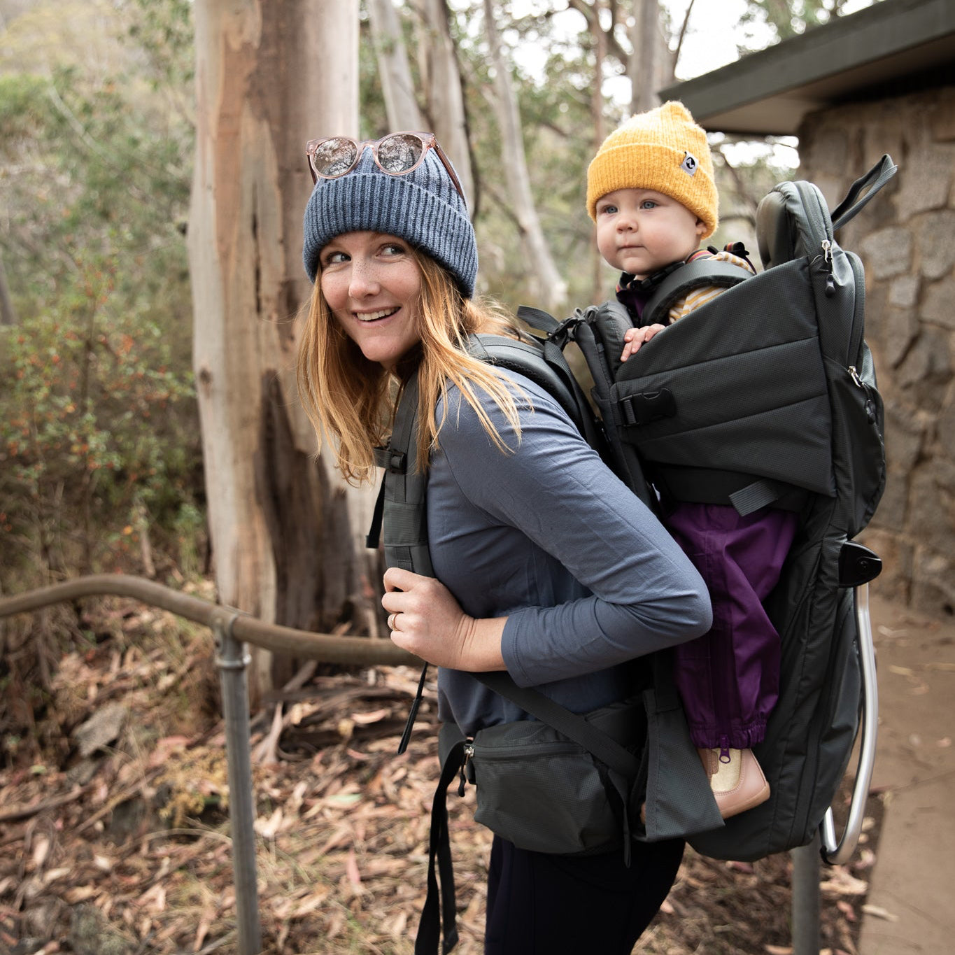 Woman carrying a child in a backpack carrier outdoors near trees